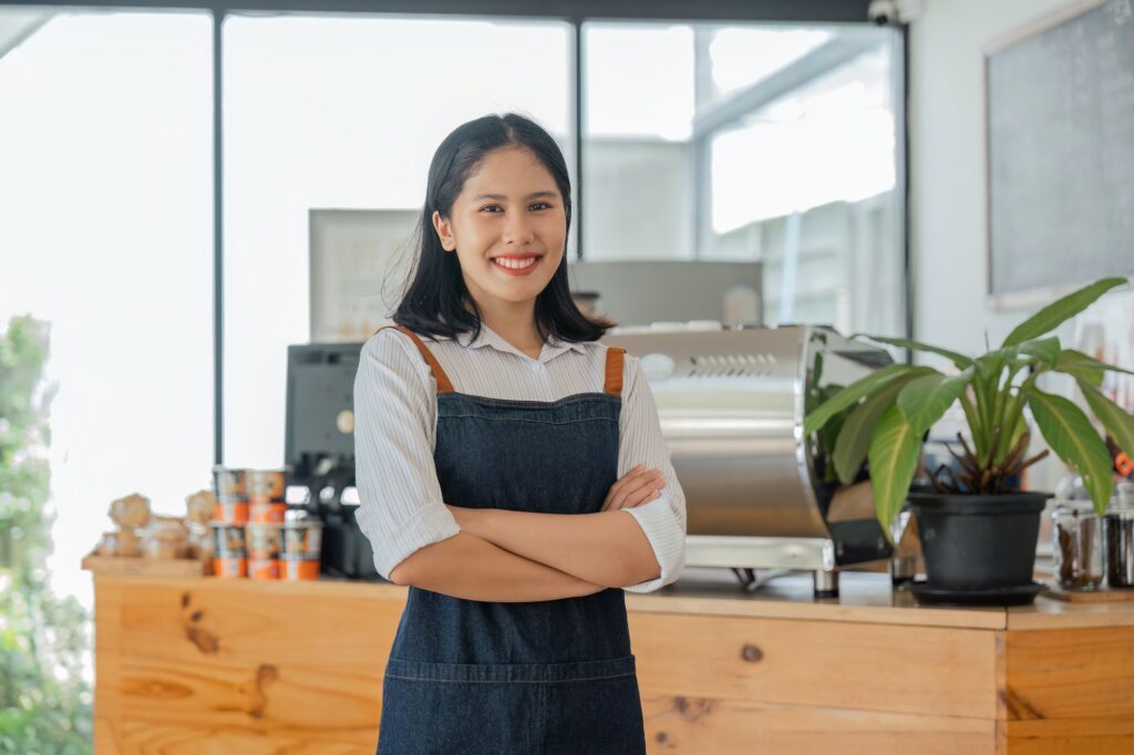 Asian woman coffee shop employee barista working at cafe. Smiling female waitress cashier. Small