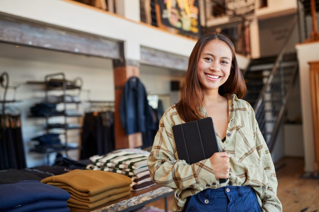 Portrait Of Female Owner Of Fashion Store Using Digital Tablet To Check Stock In Clothing Store